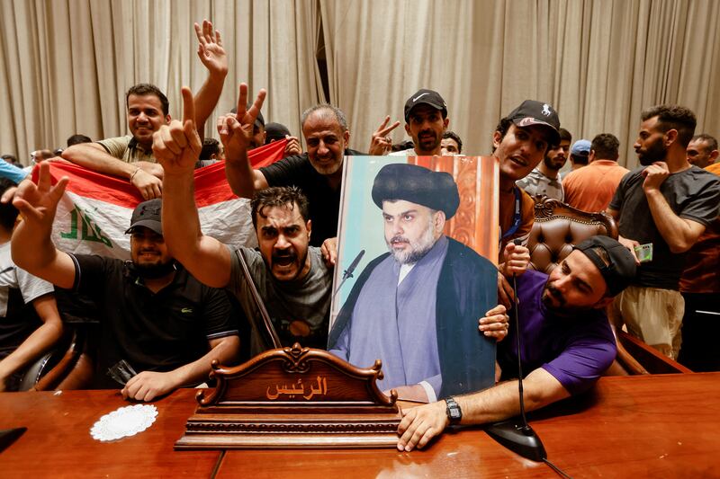 Protesters raise flags and a portrait of Mr Al Sadr. Reuters