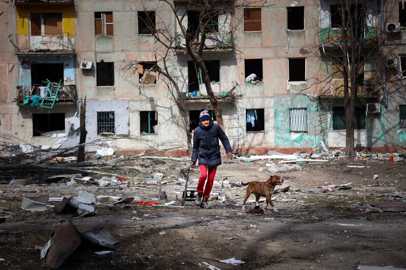 A man walks with his dog near an apartment building damaged by shelling from fighting on the outskirts of Mariupol. AP Photo