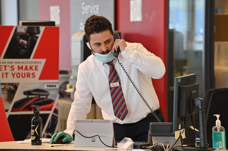 A sales person (R) wearing PPE (personal protective equipment) as a precautionary measure against COVID-19, speaks on a phone at a recently re-opened Vauxhall car dealership in north London on June 4, 2020, as lockdown restrictions are eased during the noel coronavirus COVID-19 pandemic. Car showrooms in England reopened this week as the UK government eased COVID-19 lockdown measures that have slammed the brakes on the industry. / AFP / JUSTIN TALLIS
