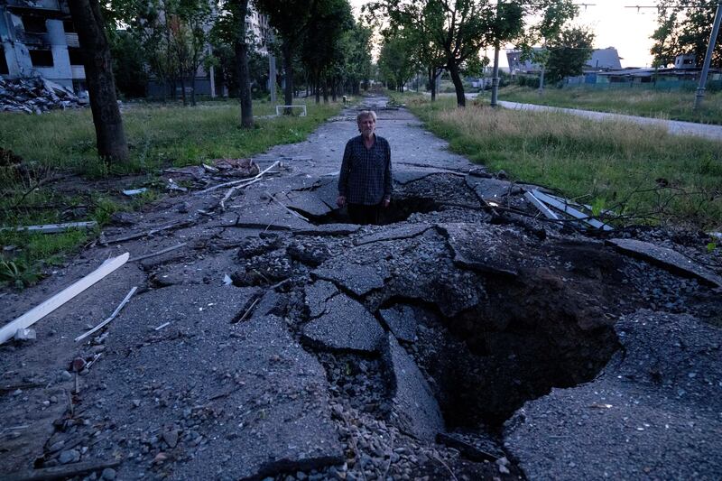 Viktor Shevchenko stands in a crater to show its depth after a Russian shelling in the Saltivka district in Kharkiv. AP