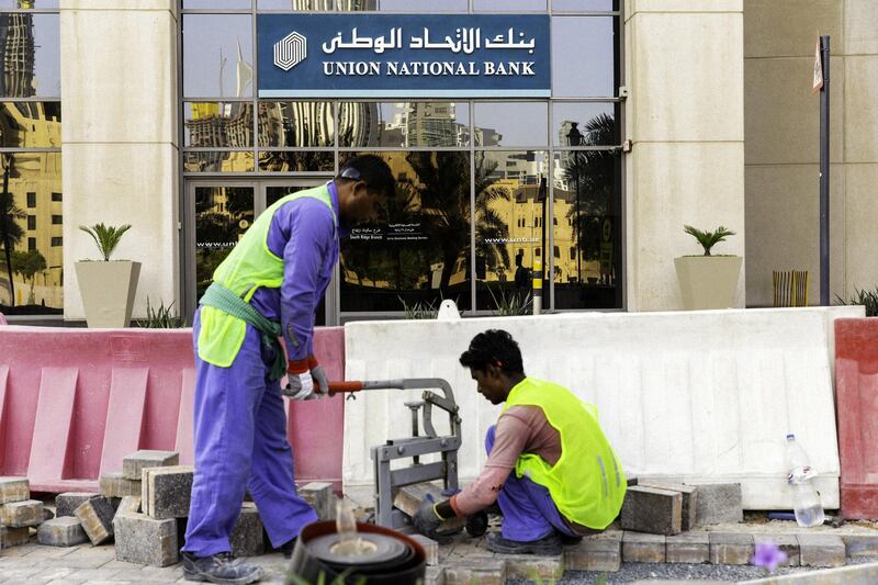 Workers cut bricks to lay a sidewalk outside a Union National Bank PJSC bank branch in Dubai, United Arab Emirates, on Tuesday, Sept. 4, 2018. Abu Dhabi is engineering a second bank merger in its latest attempt to stay competitive in the era of lower oil prices. Photographer: Christopher Pike/Bloomberg