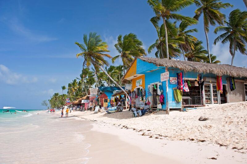 Punta Cana, Dominican Republic- July 20, 2013:  Tourist walking on the beach and take a tour of the bungalows-stalls with souvenirs. Locals sitting in front of stalls
