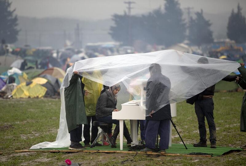 Syrian pianist Nour Alkhzam, center left, plays the piano as Chinese dissident artist Ai WeiWei, center right, holds a plastic sheet, along with other people, during a heavy rain at the northern Greek border station of Idomeni on March 12, 2016. Vadim Ghirda/AP Photo