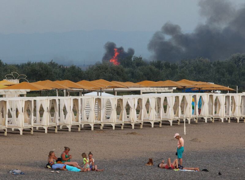 People rest on a beach as smoke and flames rise after explosions at a Russian military air base in Novofedorivka, Crimea, on Tuesday. Reuters