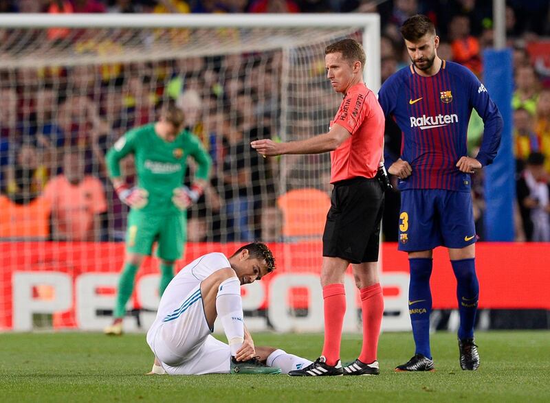 TOPSHOT - Real Madrid's Portuguese forward Cristiano Ronaldo (L) sits on the field after resulting injured dbeside Spanish referee Hernandez Hernandez (C) and Barcelona's Spanish defender Gerard Pique uring the Spanish league football match between FC Barcelona and Real Madrid CF at the Camp Nou stadium in Barcelona on May 6, 2018. / AFP PHOTO / Josep LAGO