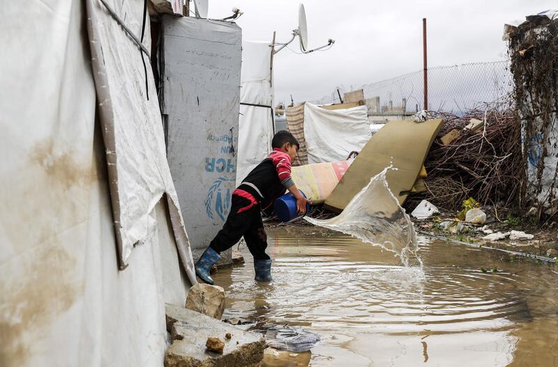 TOPSHOT - A Syrian child uses a bucket to bale out water from his tent at a refugee camp on the outskirts of the town of Zahle in Lebanon's Bekaa Valley on January 26, 2018.
Lebanon, a country of four million, hosts just under a million Syrians who have sought refuge from the war raging in their neighbouring homeland since 2011, many of whom live in informal tented settlements in the country's east and struggle to stay warm in the winter. / AFP PHOTO / JOSEPH EID