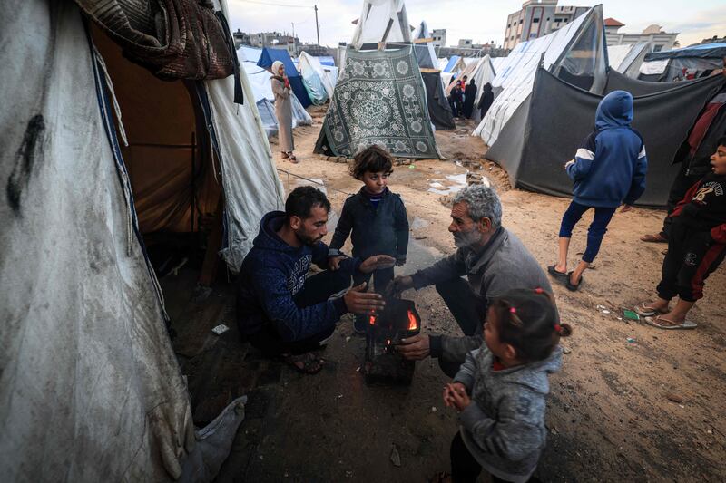 Displaced Palestinians warm up around a fire at a makeshift camp. AFP