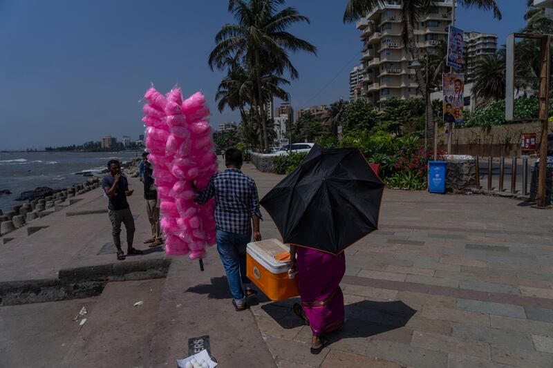 A man selling candy floss in Mumbai helps a water vendor who is using an umbrella as a parasol. AP