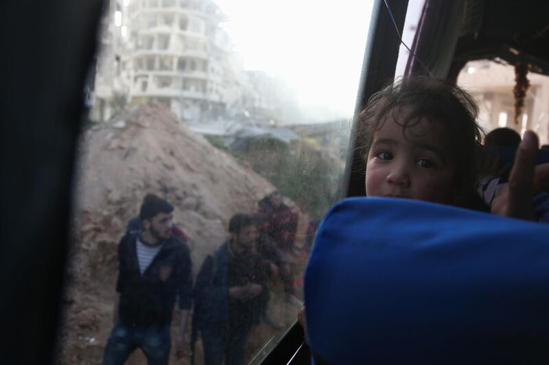 A convoy transporting Syrian civilians and rebel fighters drives past destroyed buildings in Arbin in Eastern Ghouta as they are evacuated from the opposition enclave to the village of Qalaat al-Madiq, some 45 kilometres northwest of the central city of Hama, on March 25, 2018. Abdulmonam Eassa / AFP