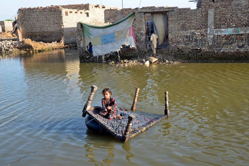 A girl sits on a cot as she crosses a flooded street in the Jaffarabad district, Balochistan province, Pakistan. AFP