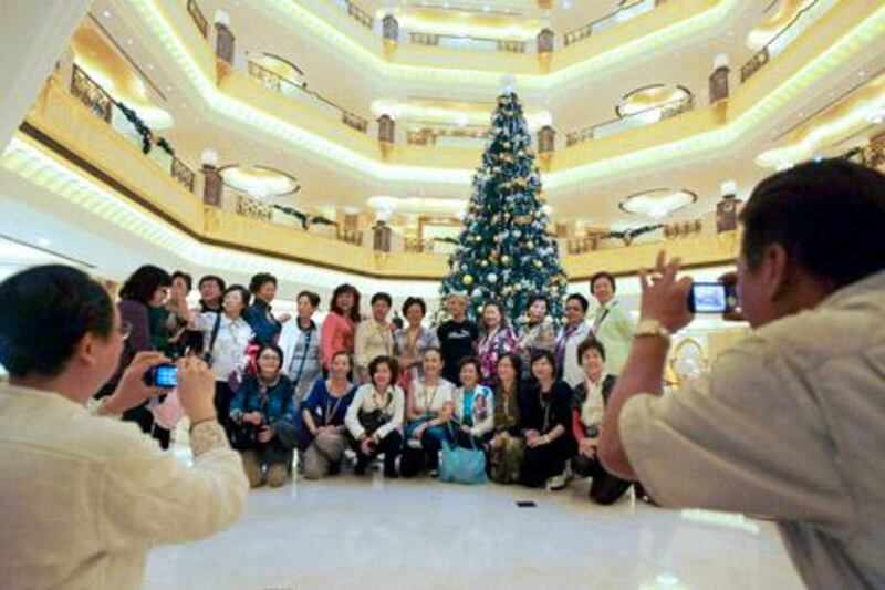 Tourists pose to have their photos taken in front of a Christmas tree which has been decked out with dollars 11 million U.S. (14.3 million euro) worth of gold, at the Emirates Palace hotel, in Abu Dhabi, United Arab Emirates, on Thursday Dec. 16, 2010.  The hotel's general manager, Hans Olbertz, was quoted in local newspapers Thursday as saying the 43-foot (13-meter) faux fir has 131 ornaments that include gold and precious stones including diamonds and sapphires. The $11 million symbol of the season has become the latest extravagance at the Emirates Palace hotel, which boasts its own marina, heliport and a vending machine that pops out small gold bars.(AP Photo/Hussein Malla)