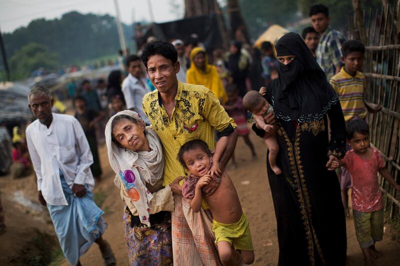 FILE - In this Sept. 5, 2017, file photo, an exhausted Rohingya helps an elderly family member and a child as they arrive at Kutupalong refugee camp after crossing from Myanmmar to the Bangladesh side of the border, in Ukhia. Myanmar, a predominantly Buddhist nation of 60 million, was basking in international praise just a few years ago as it transitioned to democracy after a half-century of dictatorship. Since then, a campaign of killings, rape and arson attacks by security forces and Buddhist-aligned mobs have sent more than 850,000 of the country's 1.3 million Rohingya fleeing. (AP Photo/Bernat Armangue, File)