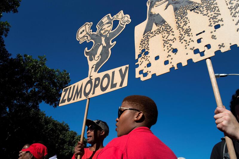 People carry a placard with a parody of one of the Gupta brothers during a demonstration march organised by a broad-based coalition called #UniteBehind, to place pressure on MPs to vote for the removal of South African President Jacob Zuma (not visible) before a no-confidence vote by parliament, on August 7, 2017 in Cape Town.  
A coalition, including members of most of South Africa's political opposition parties, churches, unions, and other civic organisations marched on August 7 calling for the removal of president Jacob Zuma. Zuma faces increasing opposition, even within his own party, the ruling African National Congress (ANC), about his connection to the Gupta family of businessmen, and South Africa's downgrading by financial rating agencies.  / AFP PHOTO / RODGER BOSCH