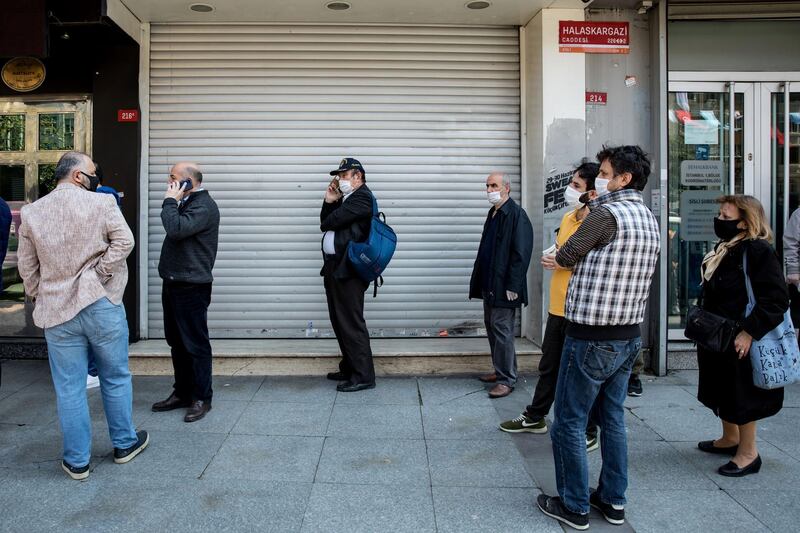 Customers wearing protective face masks maintain social distancing while queuing before the opening of a bank branch in Istanbul, Turkey, on Monday, April 27, 2020. Coming off a brief recession just over a year ago, the urgency is mounting for Turkey to loosen the screws on the economy as its currency and reserves come under pressure more than a month after it introduced social-distancing measures. Photographer: Kerem Uzel/Bloomberg