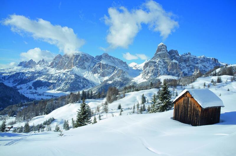 The mountains of Lavarella, Conturines and Sassongher rise high behind a snow-covered wooden barn at the Alta Badia ski resort in Corvara in the Dolomites, Südtirol, Italy, which offers a multitude of skiing and dining delights. Ellen Rooney