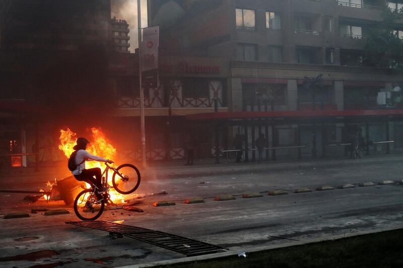 A demonstrator rides a bicycle past a bonfire in Santiago, Chile. Reuters