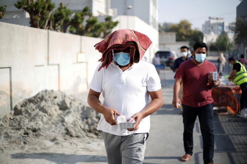 People wear face masks and maintain physical distancing as they collect their free Ramadan meals from volunteers of Adliya Charity in Manama, Bahrain. Reuters