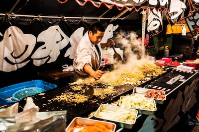 Tokyo, Japan - October 12, 2012: Man cooking in food market stall at Oeshiki festival in Tokyo Japan. This Buddhist festival is celebrated in October every year in many places in Japan. But the one portrayed in the picture that goes from the Ikejami train station to Ikejami Honmonji temple is the most famous one. More than 300.000 people congregate on this night to commemorate High Priest Nichiren death more than 700 years ago. People of all ages carry big portable shrines decorated with paper lanterns that resemble cherry blossom and dance play music and sing. The parade ends at the Honmonji temple where it is believed is the place where Nichire died.