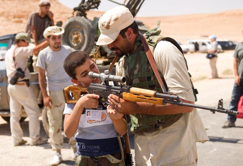 An anti-Kadhafi fighter allows a young boy to look through the view finder of his rifle on the road to Bani Walid on September 12, 2011, as civilians poured out of the Libyan oasis town fearful of new fighting between Moamer Kadhafi's forces and besieging government troops. AFP PHOTO/LEON NEAL
 *** Local Caption ***  812811-01-08.jpg