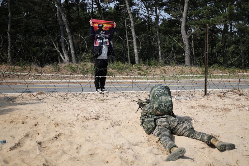 An anti-war activist holds up a sign reading "Stop war exercise, go home" in front of a marine taking up position in a military drill in Pohang, South Korea. Reuters