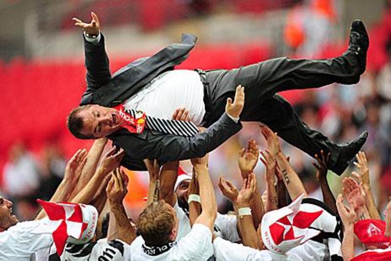 Swansea City players celebrate promotion by throwing their manager Brendan Rodgers into the air.