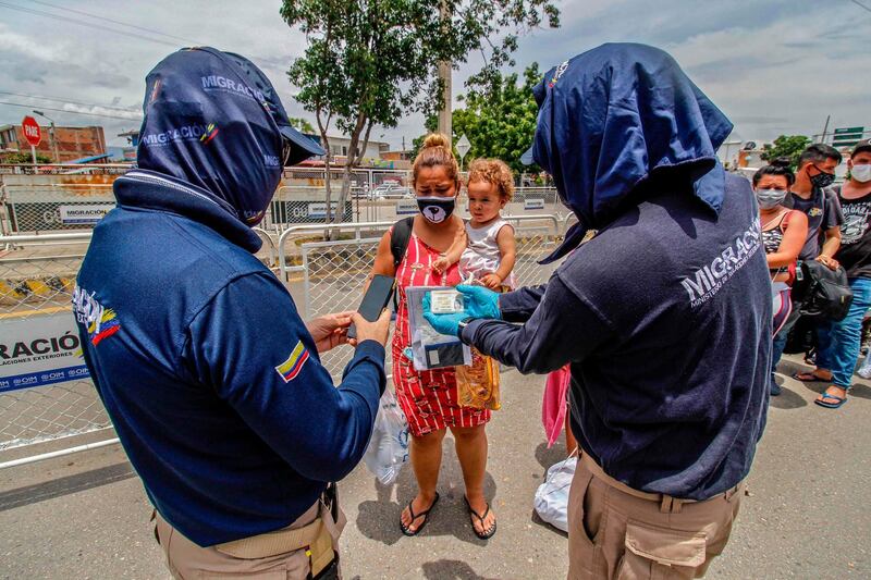 Colombian migrations officials check the document of a Venezuelan returning home with a toddler on the Simon Bolivar International Bridge, in Cucuta, Colombia, on the border with Venezuela, amid the coronavirus pandemic. AFP