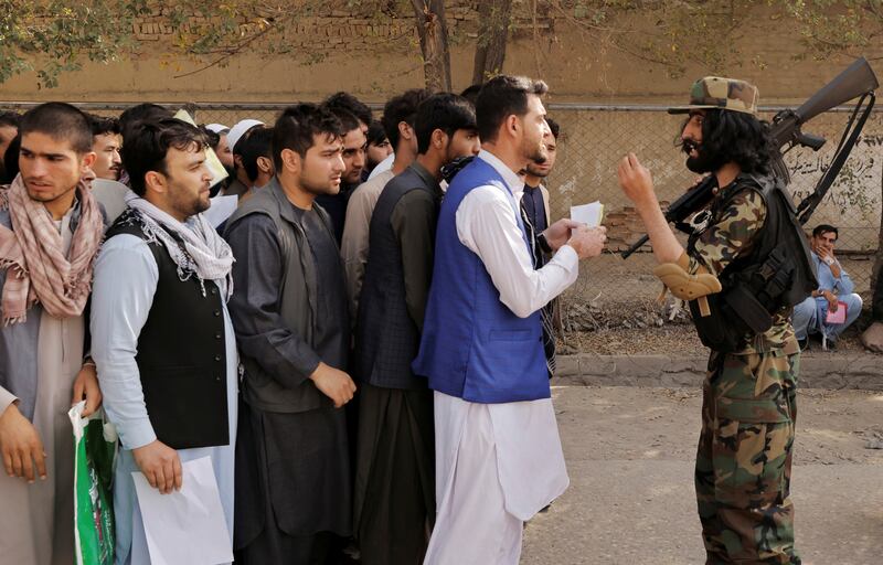 A Taliban fighter speaks to Afghans gathered outside the passport office in Kabul. Photo: Reuters