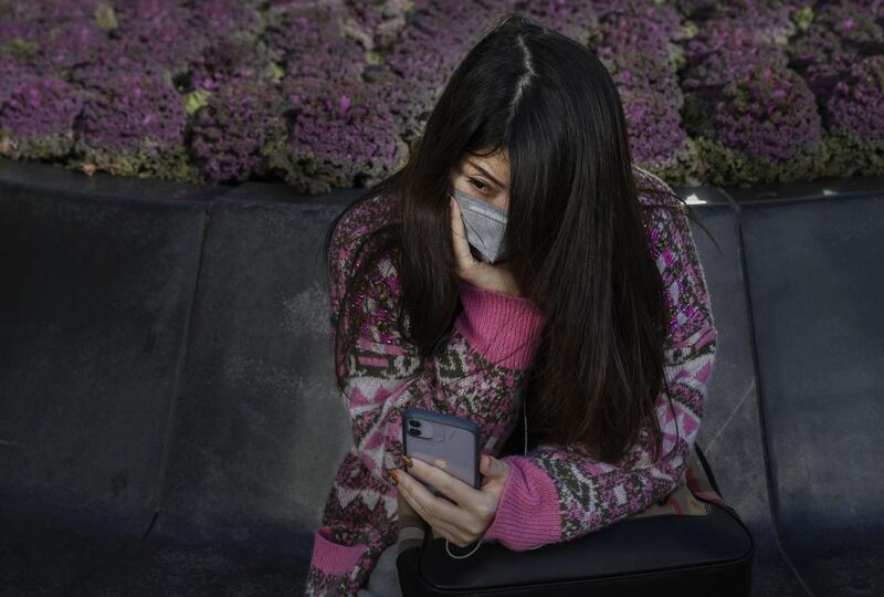 BEIJING, CHINA - MARCH 10: A Chinese woman wears a protective mask as she looks at her phone while sitting in the Sanlitun shopping area on March 10, 2020 in Beijing, China. The number of cases of the deadly new coronavirus COVID-19 being treated in China dropped to below 18,000 in mainland China Sunday, in what the World Health Organization (WHO) declared a global public health emergency last month. China continued to lock down the city of Wuhan, the epicentre of the virus, in an effort to contain the spread of the pneumonia-like disease. Officials in Beijing have put in place a mandatory 14 day quarantine for all people returning to the capital from other places in China and countries with a large number of cases like South Korea and Japan. The number of those who have died from the virus in China climbed to over 3140 on Tuesday, mostly in Hubei province, and cases have been reported in many other countries including the United States, Canada, Australia, Japan, South Korea, India, Iran, Italy, the United Kingdom, Germany, France and several others. The World Health Organization has warned all governments to be on alert and raised concerns over a possible pandemic. Some countries, including the United States, have put restrictions on Chinese travellers entering and advised their citizens against travel to China.(Photo by Kevin Frayer/Getty Images)