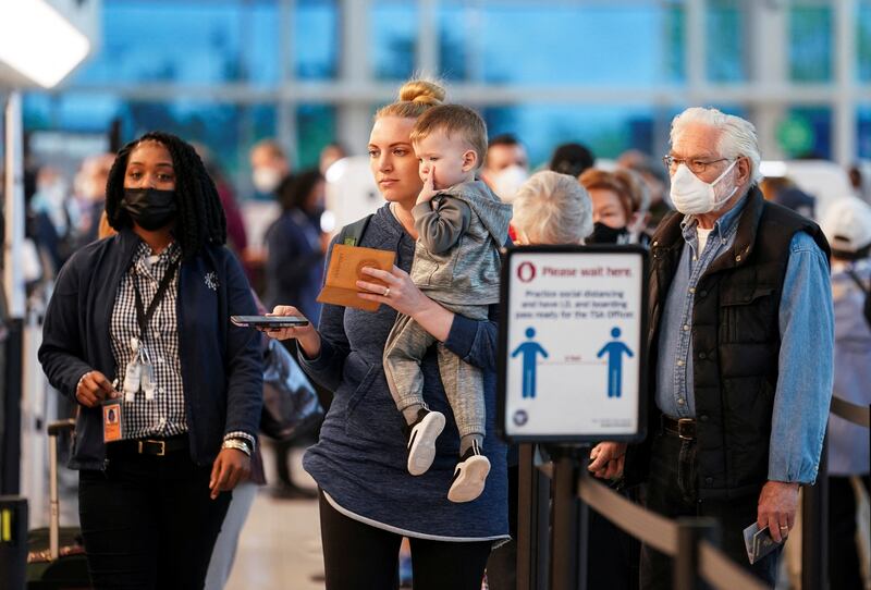 Masked and unmasked travelers line up at an airport security checkpoint after the Biden administration announced it would no longer enforce a US mask mandate on public transportation on April 19, 2022. Reuters