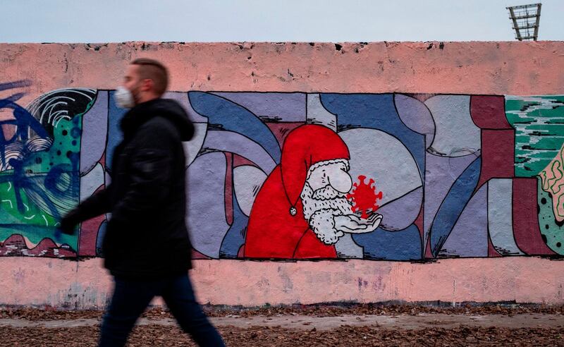 A man wearing a face mask walks past a mural painting featuring a likeness of Santa Claus holding a SARS-CoV-2 molecule, in Berlin. AFP