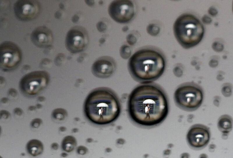 Rain drops on a car window reflect a man walking past a stock index board in Tokyo. Toru Hanai / Reuters