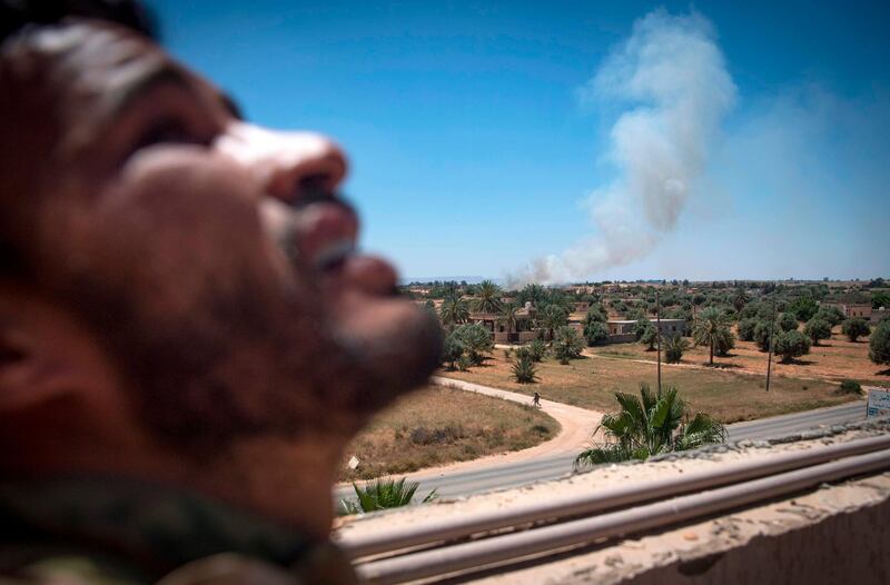 A fighter loyal to the internationally-recognised Government of National Accord (GNA) stands on a rooftop as smoke rises in the distance during clashes with forces loyal to strongman Khalifa Haftar, in Espiaa, about 40 kilometres (25 miles) south of the Libyan capital Tripoli on April 29, 2019.  Fierce fighting for control of Libya's capital that has already displaced tens of thousands of people threatens to bring a further worsening of humanitarian conditions, a senior UN official has warned. / AFP / Fadel SENNA
