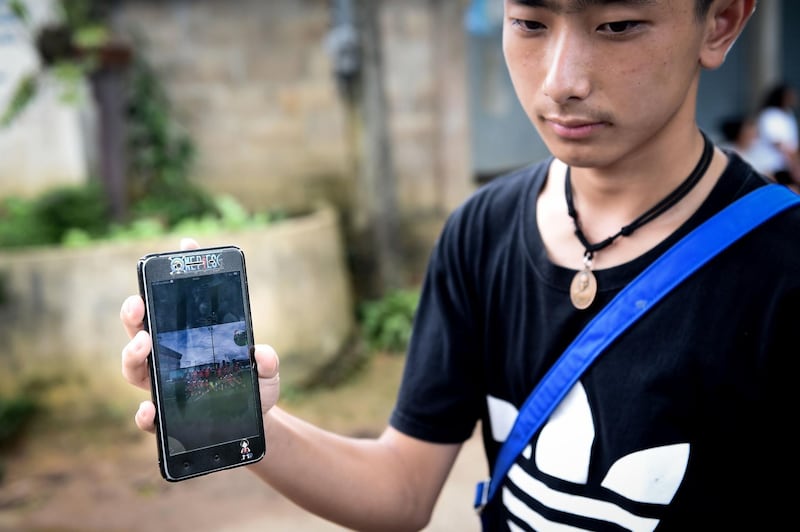 Thananchai Saengtan, 15, shows the camera a photo of his missing friends, at a football pitch near Tham Luang cave. Lillian Suwanrumpha / AFP