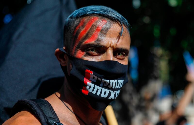 A face-painted Israeli protester wearing a protective mask amid the COVID-19 pandemic poses for a picture during a rally against Israeli Prime Minister Benjamin Netanyahu outside his official residence in Jerusalem, on July 17, 2020. His poll numbers are sinking, protests are growing and economically punishing restrictions have just been reimposed: surging coronavirus cases in Israel have left Prime Minister Benjamin Netanyahu encircled by trouble. / AFP / AHMAD GHARABLI
