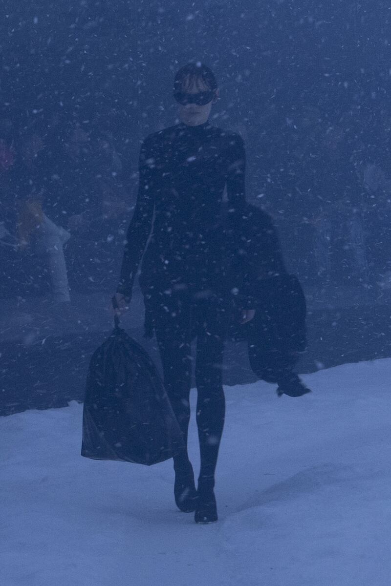 A model carries a plastic bag and a coat over her arm.