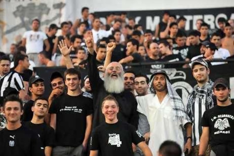 Father Christos Mitsios, a Greek Orthodox priest, centre, is instantly recognisable among the notorious Thessaloniki fans in Gate 4 of the Toumba Stadium.