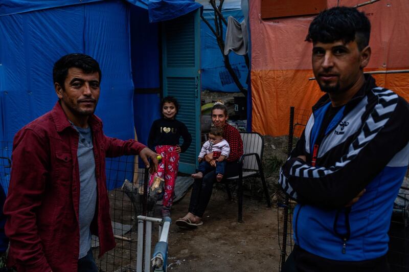 TOPSHOT - Migrants stand outside their tent near the refugee camp on the Greek island Samos, on November 13, 2019. The camp of Samos, originally built to handle 650 people, has long outstripped its boundaries. Thousands of people are now struggling to find space in the hills above the town, crafting makeshift homes out of whatever building material they can find. / AFP / ANGELOS TZORTZINIS
