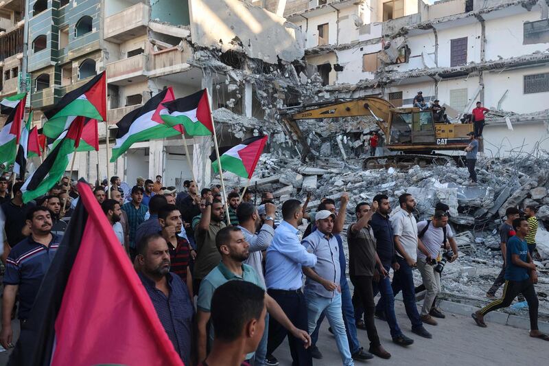 Palestinian demonstrators wave national flags in front of a building destroyed by Israeli air strikes in Gaza City on June 15, 2021, during a protest over the Israeli ultranationalist March of the Flags in Jerusalem's Old City which celebrates the anniversary of Israel's 1967 occupation of Jerusalem's eastern sector. / AFP / MOHAMMED ABED
