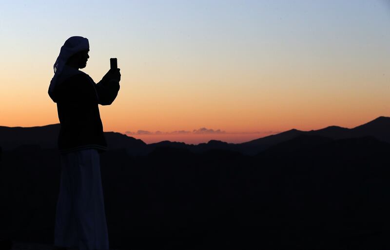 A visitor takes photos on Jebel Jais as the sun rises over Ras Al Khaimah. Pawan Singh / The National