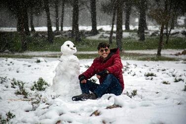 A man poses for a picture next to a snowman outside a forested area in Sidi Al Hamri. The city is in the upland Jebel Akhdar, or Green Mountain, region about 200 kilometres east of Benghazi, on February 16, 2021. AFP
