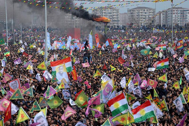 Smoke rises from a fire burning as people wave Kurdish flags and pictures of jailed Kurdish rebel leader Abdullah Ocalan as they gather to celebrate Newroz, the Kurdish New Year, in the southeastern Turkish city of Diyarbakir on March 21, 2015. Ilyas Akengin/AFP Photo


