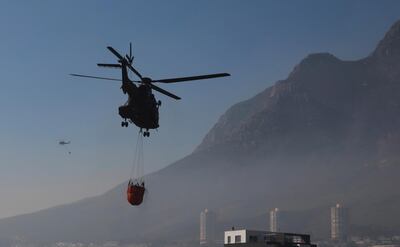 Water bombing helicopters hover by the slopes of Cape Town's, Table Mountain slopes, in South Africa,  Tuesday, April 20, 2021. Fire crews worked for a third day to extinguish a wildfire as the city came to terms with the damage caused by what officials have described as one of the area's worst blazes in years. (AP Photo/Nardus Engelbrecht)