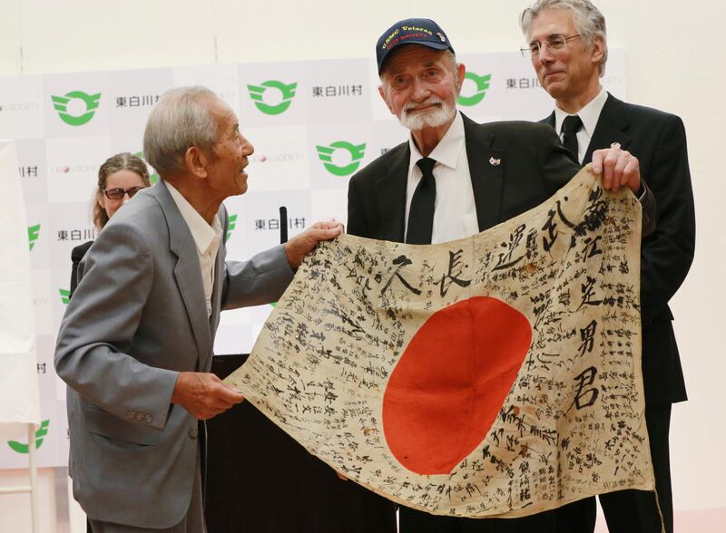 WWII veteran Marvin Strombo, second right, and Tatsuya Yasue, left, holds a Japanese flag with autographed messages which was owned by his brother Sadao Yasue, who was killed in the Pacific during World Work II, during a ceremony in Higashishirakawa, in central Japan's Gifu prefecture Tuesday, Aug. 15, 2017. (AP Photo/Eugene Hoshiko)