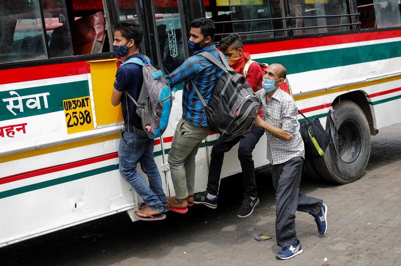 Migrant workers hang on to a door of a moving bus as they return to their villages after Delhi government ordered a six-day lockdown. Reuters