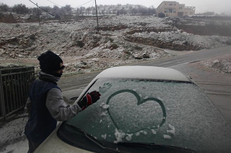 A boy makes a print of his hand on a car windscreen covered with snow before clearing it, during stormy weather in the Druze village of Majdal Shams on the Golan Heights January 8, 2013. REUTERS/Ammar Awad (ENVIRONMENT) *** Local Caption ***  JER27_ISRAEL-STORM-_0108_11.JPG