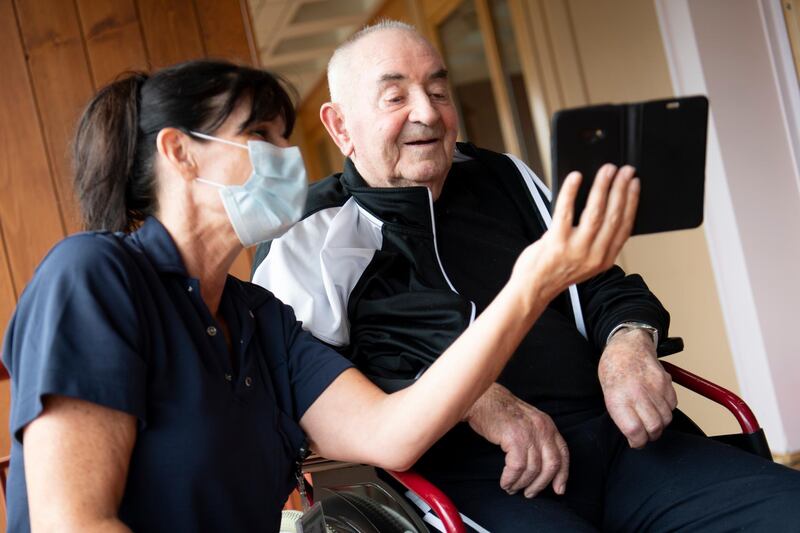 Animator Mirella Raymond, left, wearing a protective face mask, helps Marc-Henri, right, who survived Covid-19, and his family in a balcony of the retirement home in Chateau-d'Oex, Switzerland, on April 20, 2020. AP