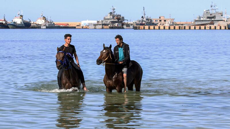Men ride horses in the Mediterranean Sea waters near the port of Libya's capital Tripoli, as they cool off in the hot weather despite a lockdown to tackle coronavirus pandemic. AFP