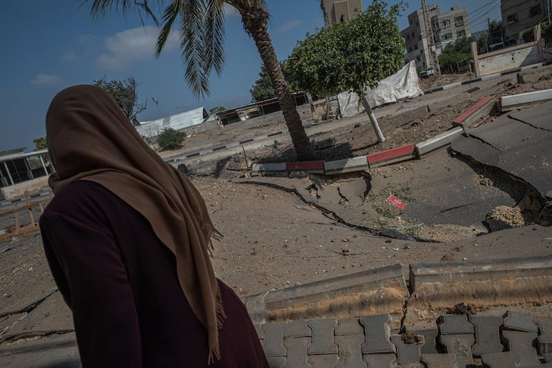 A woman walks beside a broken asphalt, after an Israeli air strike on Beit Hanoun, in the northern Gaza Strip. Getty Images