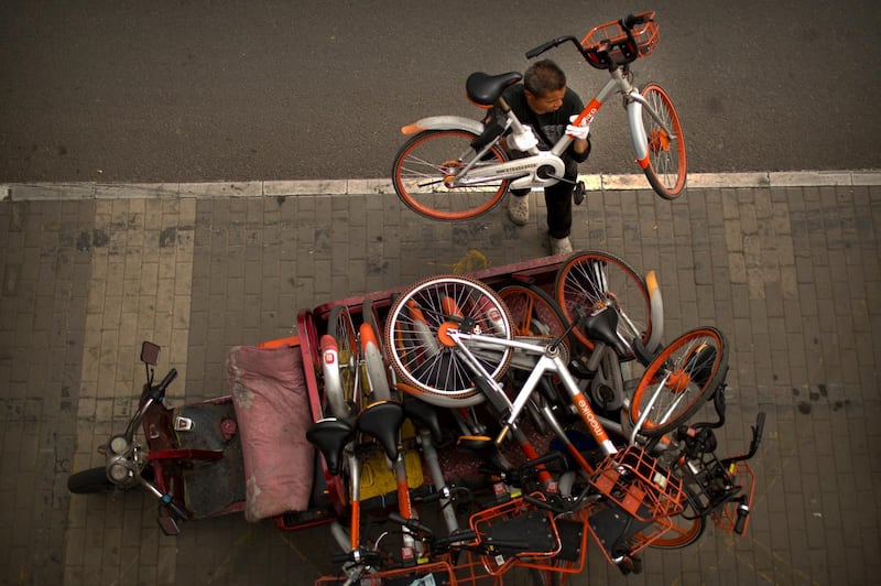 A worker lifts a shared bicycle from a stack of bicycles in the back of a cart along a street in Beijing, China, on May 16, 2018. Mark Schiefelbein / AP Photo