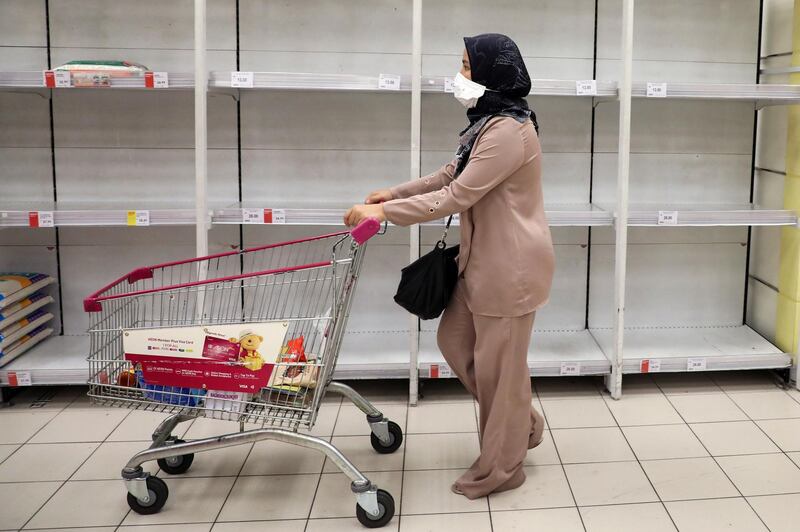 A woman wearing a protective mask walks past empty shelves at a supermarket in Kuala Lumpur, Malaysia. Lim Huey Teng / Reuters